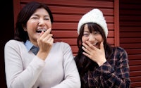 two japanese women laughing while holding their mouths open