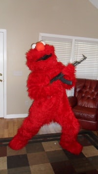 a red elmo mascot holding a gun in a living room